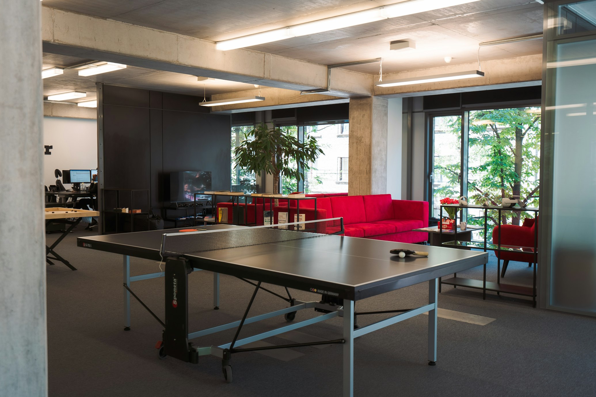 Modern office space featuring elegant furniture, glass partitions, and a stylish area with a table tennis setup for recreation.